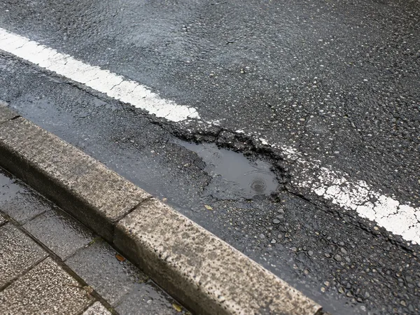 雨上がりの車道の端にできたポットホール（イメージ）
